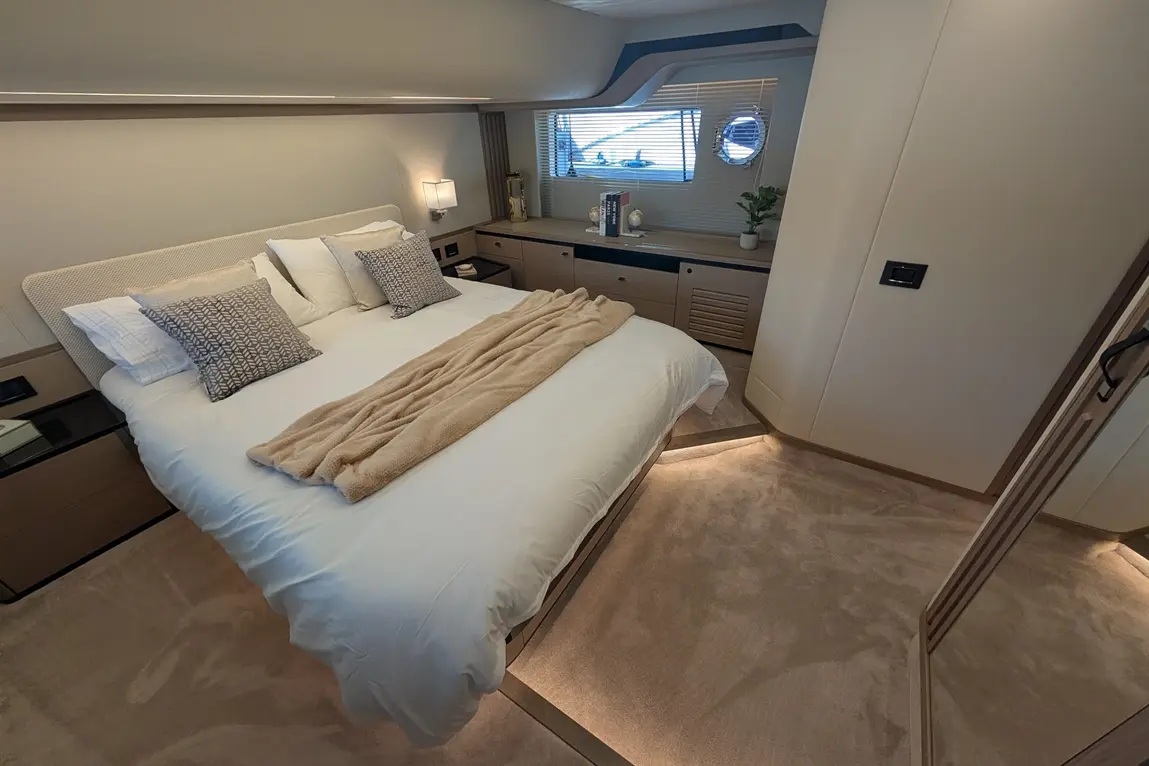 Modern bedroom with a plush king-sized bed, pillows, a light throw, sleek storage units, and a window showing a scenic view.